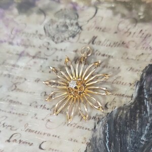 May include: A gold-toned flower pendant with a single diamond in the centre. The pendant is on a white background with cursive writing.