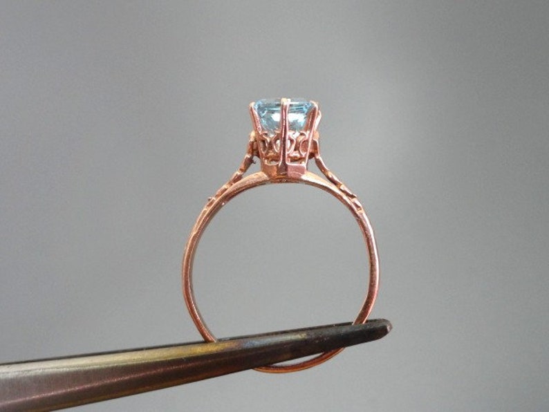 K&ouml;nnte beinhalten: Ein zarter Goldring mit einem hellblauen Edelstein, der in einer detaillierten kronenartigen Fassung sitzt.