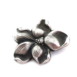 Puede incluir: Un broche de plata con forma de flor con un dise&ntilde;o detallado. La flor tiene cinco p&eacute;talos y un centro con un peque&ntilde;o c&iacute;rculo en relieve.