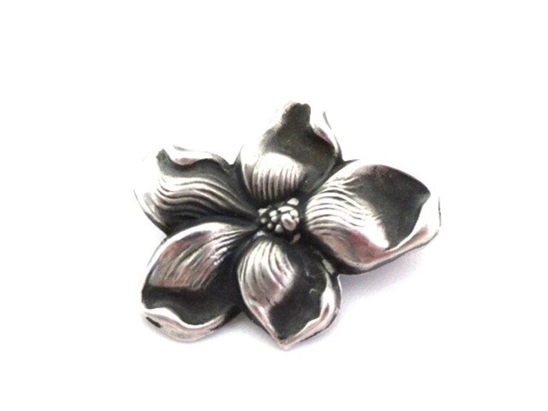 Puede incluir: Un broche de plata con forma de flor con un dise&ntilde;o detallado. La flor tiene cinco p&eacute;talos y un centro con un peque&ntilde;o c&iacute;rculo en relieve.