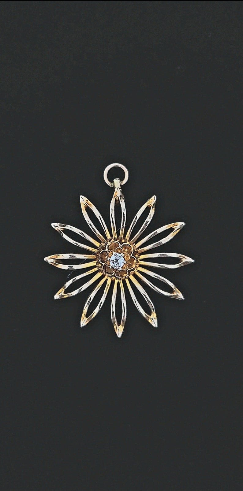 May include: A gold and silver pendant in the shape of a flower with a single clear rhinestone in the centre.