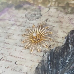 May include: A gold flower pendant featuring a single diamond at its centre. The pendant is delicate and intricate, with a starburst design.