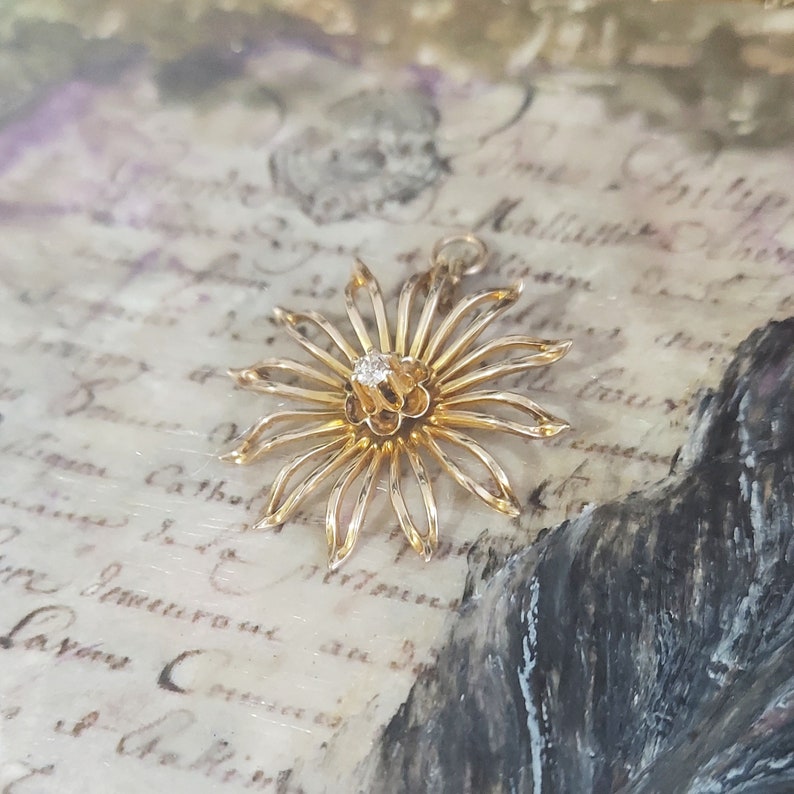 May include: A gold flower pendant featuring a single diamond at its centre. The pendant is delicate and intricate, with a starburst design.