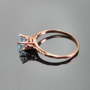 K&ouml;nnte beinhalten: Ein Ring aus Ros&eacute;gold mit einem hellblauen Edelstein, der in einem filigranen Design gefasst ist.