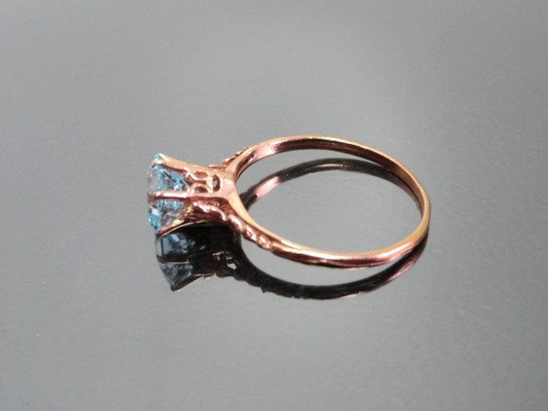 K&ouml;nnte beinhalten: Ein Ring aus Ros&eacute;gold mit einem hellblauen Edelstein, der in einem filigranen Design gefasst ist.