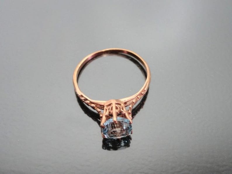 K&ouml;nnte beinhalten: Ein zarter Ring aus Ros&eacute;gold mit einem ovalen blauen Edelstein, der in einem filigranen Design gefasst ist.