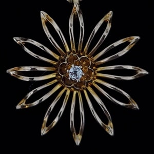 May include: A gold-toned pendant in the shape of a flower with a single diamond in the centre. The flower has 12 petals.