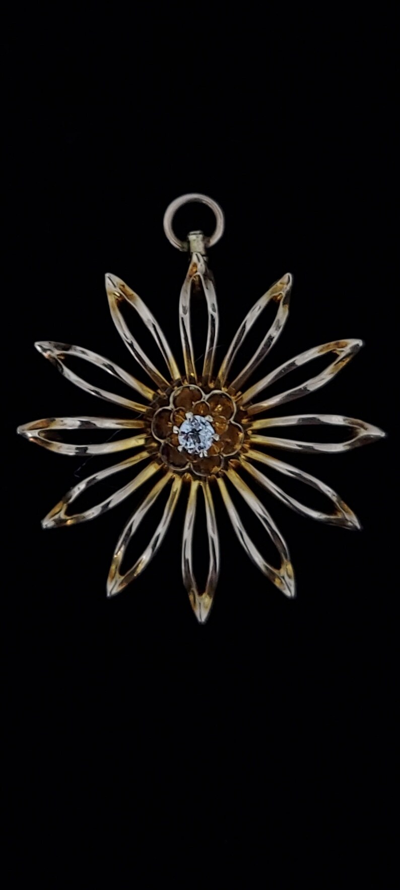 May include: A gold-toned pendant in the shape of a flower with a single diamond in the centre. The flower has 12 petals.
