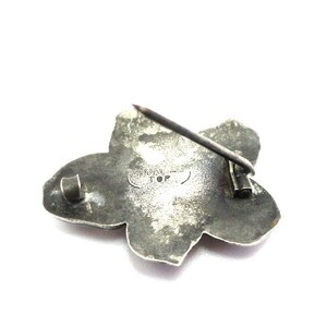 Puede incluir: Broche de plata en forma de flor con un pasador en la parte posterior. La broche tiene forma de estrella y est&aacute; marcada con "Sterling JOP".