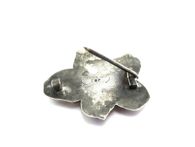 Puede incluir: Broche de plata en forma de flor con un pasador en la parte posterior. La broche tiene forma de estrella y est&aacute; marcada con "Sterling JOP".