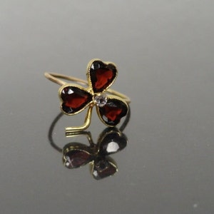 May include: A gold clover ring with three red heart-shaped gemstones and a small clear gemstone in the center.