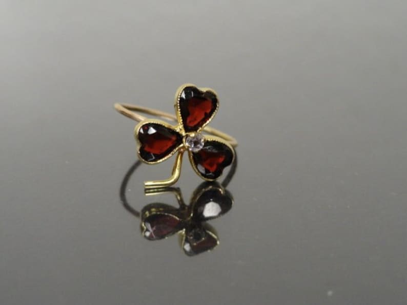 May include: A gold clover ring with three red heart-shaped gemstones and a small clear gemstone in the center.