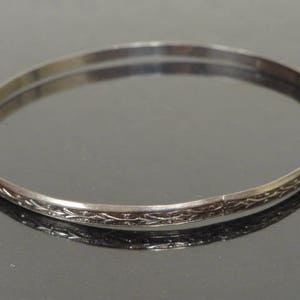 May include: A silver bangle bracelet with a delicate etched design.