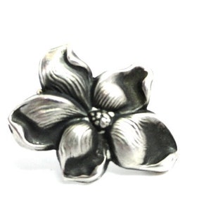 Puede incluir: Un broche de plata con forma de flor con un dise&ntilde;o texturizado detallado.