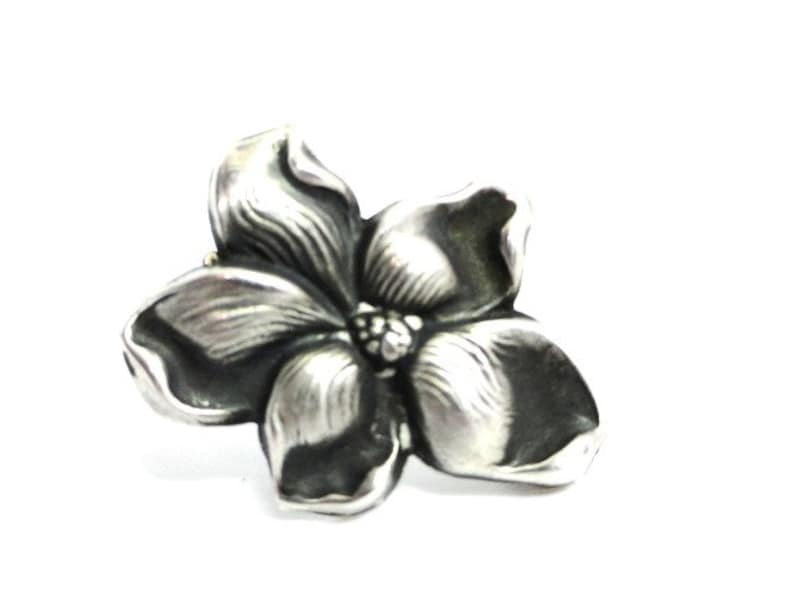 Puede incluir: Un broche de plata con forma de flor con un dise&ntilde;o texturizado detallado.