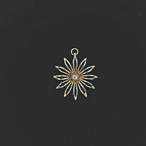 May include: A gold pendant in the shape of a flower with a single clear gemstone in the centre.