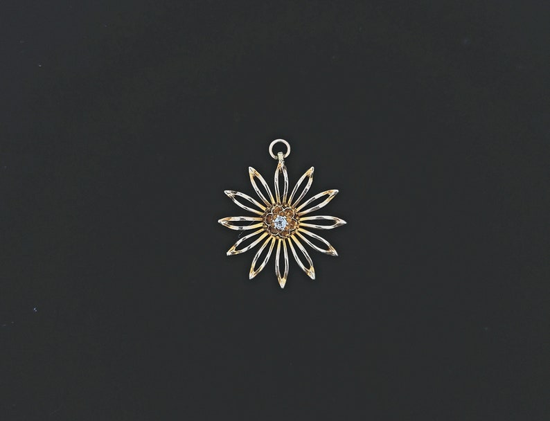 May include: A gold pendant in the shape of a flower with a single clear gemstone in the centre.
