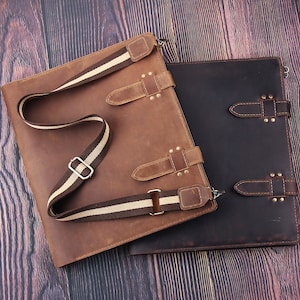 Può includere: Due borse a tracolla in pelle marrone e marrone scuro. La borsa marrone chiaro ha una tracolla a righe e cinturini in pelle con fibbie. La borsa scura ha cinturini con fibbia simili. Entrambe sono su una superficie di legno.