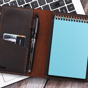 May include: A brown leather notebook with a pen, a card holder, and a blue notepad. The notebook has the name "Aliza" embossed on the front.