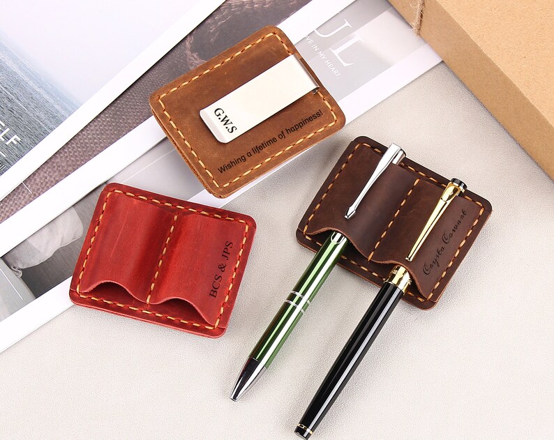 May include: Three leather card holders with personalized engravings. The first holder is brown with a money clip and the text "G.W.S. Wishing a lifetime of happiness!" The second holder is red with two slots and the text "BCS & JPS". The third holder is brown with two slots and the text "Coyska Cowast".