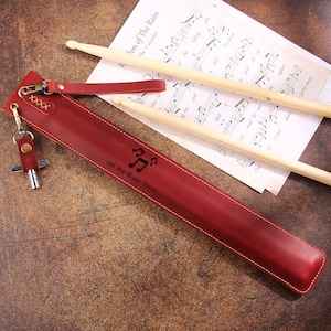 Peut inclure: Un &eacute;tui &agrave; baguettes en cuir rouge avec un porte-cl&eacute;s et un motif de note de musique. L'&eacute;tui porte la gravure "Let the Music Speak".