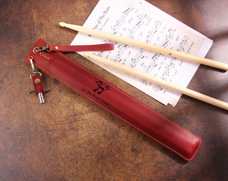 Peut inclure: Un &eacute;tui &agrave; baguettes en cuir rouge avec un porte-cl&eacute;s et un motif de note de musique. L'&eacute;tui porte la gravure "Let the Music Speak".