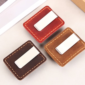 May include: Three leather money clips with metal clasps. The clips are brown, red, and tan.