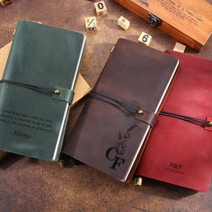 May include: Three leather journals in green, brown, and red. The green journal has the text "I love those days when my only decision is whether to go to the beach in the morning or afternoon -Mimo-". The brown journal has the initials "CF" and a floral design. The red journal has the initials "P&F" and the date "11.25.2024".