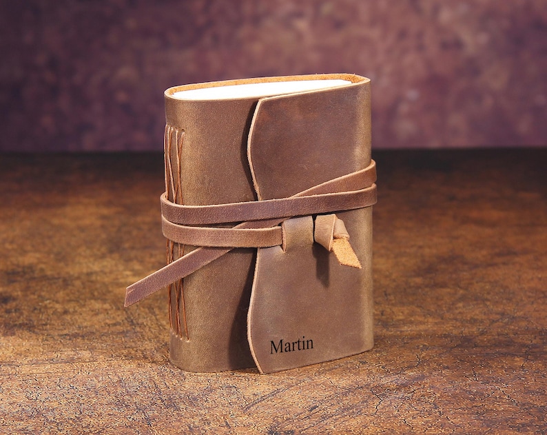 May include: A brown leather journal with a leather strap closure and the name "Martin" embossed on the front.