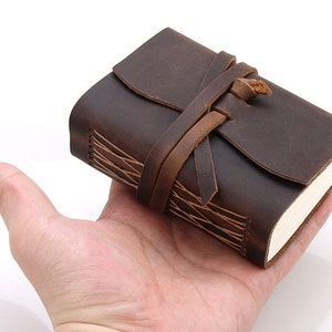 May include: A brown leather-bound journal with a leather strap closure. The journal has a rustic, vintage look and is perfect for writing or sketching.