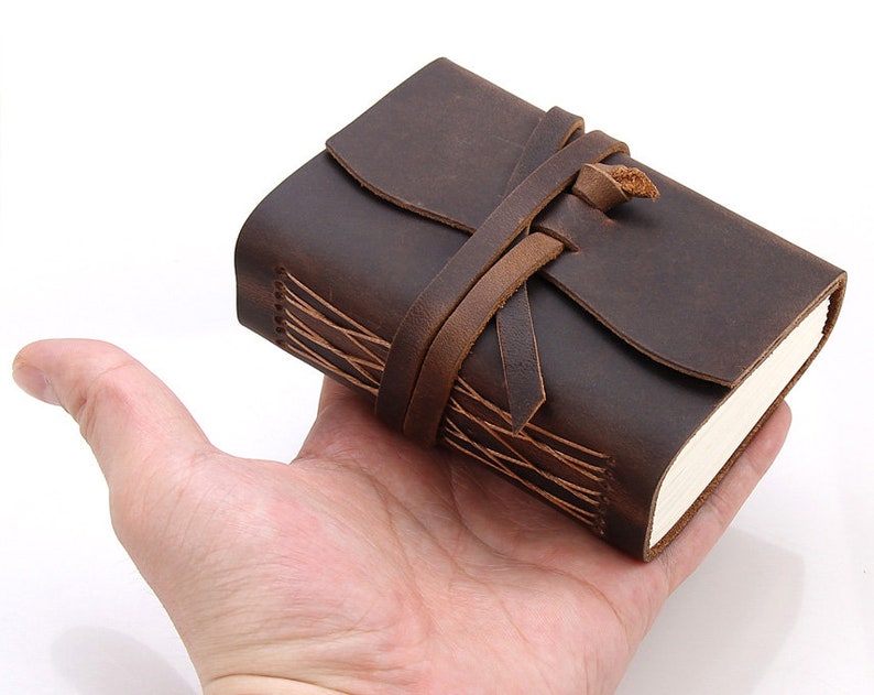 May include: A brown leather-bound journal with a leather strap closure. The journal has a rustic, vintage look and is perfect for writing or sketching.