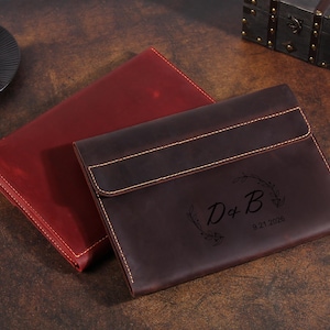 May include: Two rectangular leather document folders with flap closures and visible stitching. One folder is deep red, and the other is dark brown with an engraved floral wreath design featuring the letters D & B and the date 9.21.2028.
