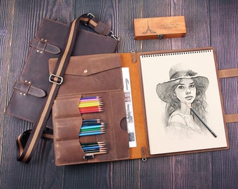 Pode incluir: Um portfólio de couro castanho com uma correia e um porta-lápis. O portfólio contém um bloco de desenho com um desenho de uma mulher de cabelo comprido usando um chapéu.