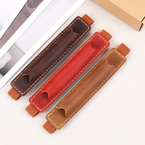 May include: Three leather pen holders in brown, red, and tan. Each holder has a stitched seam and an elastic band at each end.