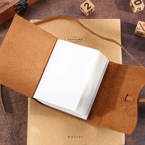 May include: A brown leather bound journal with blank pages. The journal is open and lying on a brown surface. The journal has a strap closure and a decorative metal clasp.
