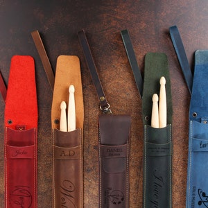 Peut inclure: Cinq porte-baguettes en cuir personnalis&eacute;s de diff&eacute;rentes couleurs et avec des noms. Les porte-baguettes sont en cuir marron, rouge, vert, bleu et noir. Chaque porte-baguettes a une sangle et une poche pour les baguettes. Les noms sur les porte-baguettes sont Jackie, A.D., Daniel, Je t'aime et Barry.
