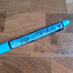 Op de afbeelding: Een blauwe pen met een wit en blauw bloemenontwerp en de tekst "Grüße aus Tirol Austria" in zwart.