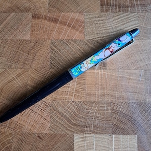 Può includere: Una penna nera e blu con un design di personaggio dei cartoni animati. Il personaggio è una figura blu e bianca con un fulmine giallo. La penna ha il testo "The Flintstones" su di essa.