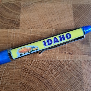 Könnte beinhalten: Ein blauer und gelber Stift mit einem Cartoon-Bild eines Sattelzuges, der einen Tankwagen zieht. Der Stift trägt die Aufschrift "IDAHO".