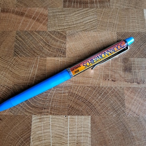 Op de afbeelding: Een blauwe pen met een geel en oranje label met de tekst "National Park Schiermonnikoog".