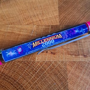 Könnte beinhalten: Ein rosa-blauer Stift mit einer silbernen Klammer. Der Stift hat ein Feuerwerksdesign und den Text "Millennium 2000 A celebration of the past, present and future".