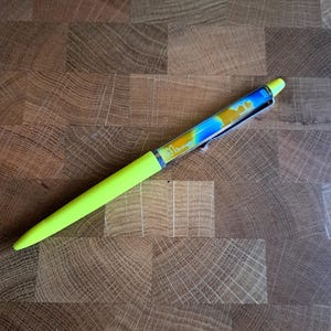 Op de afbeelding: Een felgele pen met een transparant lichaam gevuld met blauwe en gele vloeistof. De pen heeft een zwarte clip en de woorden "Bic Cristal" staan ​​gedrukt op de zijkant.