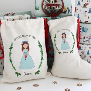 May include: A beige drawstring gift bag and a matching Christmas stocking, both featuring a printed illustration of a girl in a light blue dress holding a nutcracker, surrounded by a holly wreath and the text Special Delivery For Clara.