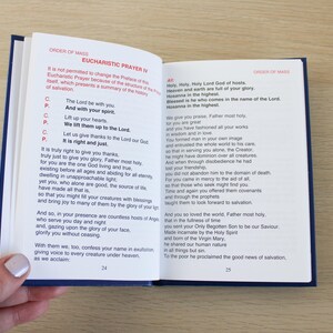 K&ouml;nnte beinhalten: Offenes Buch mit blauem Einband, das den Text aus dem Mess-Ordo, Eucharistisches Hochgebet IV, zeigt. Wei&szlig;e Seiten mit schwarzem Text. Eine Hand h&auml;lt das Buch auf einer hellen Holzoberfl&auml;che offen.