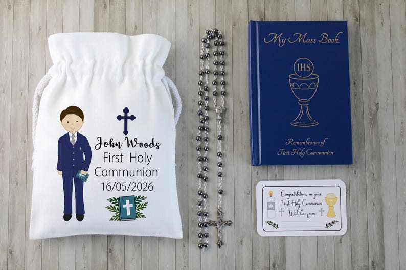 K&ouml;nnte beinhalten: Ein Erstkommunion-Set mit einem wei&szlig;en Kordelzugbeutel mit einer Jungenillustration und Text, einem Rosenkranz, einem blauen Buch mit goldener Schrift und einer Karte. Der Beutel tr&auml;gt den Namen "John Woods" und das Datum 16.05.2026.