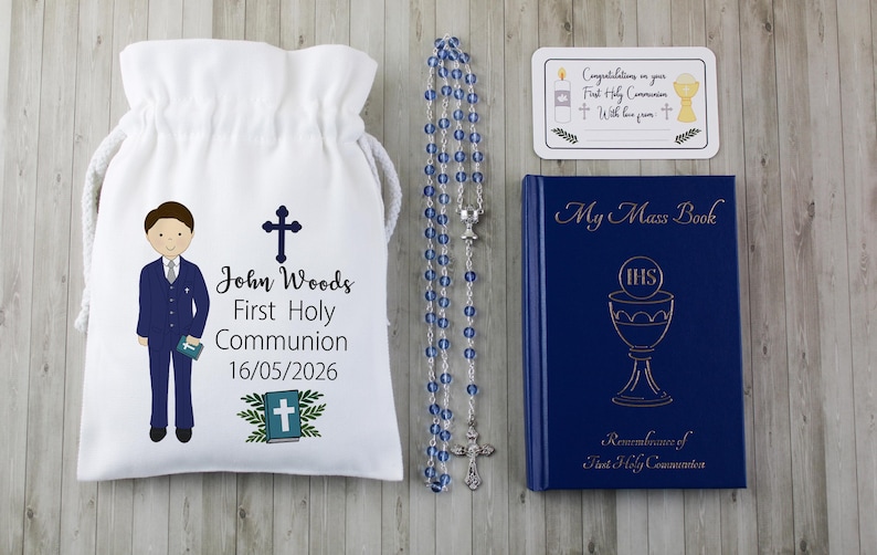 K&ouml;nnte beinhalten: Ein Erstkommunion-Set mit einem wei&szlig;en Kordelzugbeutel mit einer Jungenillustration und Text, einem Rosenkranz mit blauen Perlen, einem blauen Buch und einer Karte. Der Beutel tr&auml;gt den Namen "John Woods" und das Datum 16.05.2026.