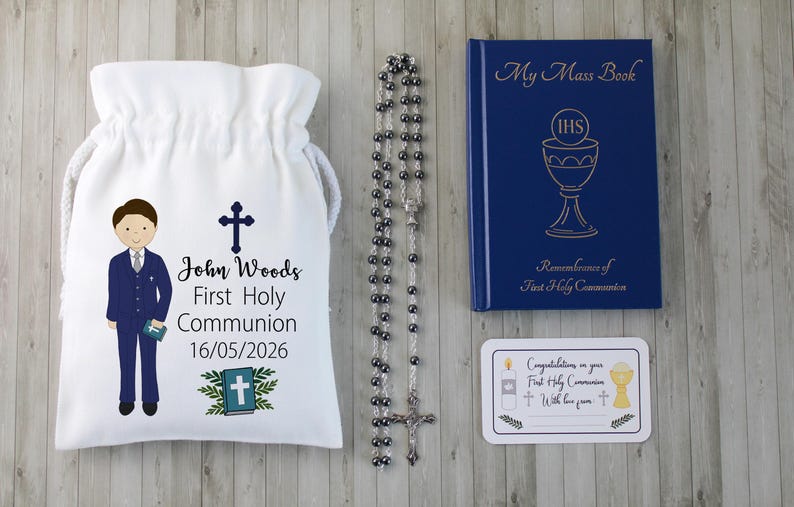 K&ouml;nnte beinhalten: Ein Erstkommunion-Set mit einem wei&szlig;en Kordelzugbeutel mit einer Jungenillustration und dem Namen "John Woods". Enth&auml;lt einen Rosenkranz, ein blaues "My Mass Book" und eine Gl&uuml;ckwunschkarte. Das Datum "16/05/2026" ist auf der Tasche aufgedruckt.