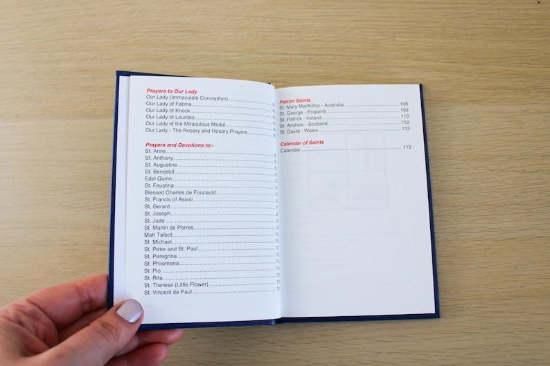 K&ouml;nnte beinhalten: Ein offenes Buch mit blauem Einband, das eine Liste von Gebeten und Andachten zeigt. Der Text enth&auml;lt "Gebete zu Unserer Lieben Frau" und "Gebete und Andachten zu". Das Buch wird von einer Hand gehalten.