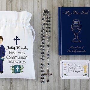 K&ouml;nnte beinhalten: Ein Erstkommunion-Set mit einem wei&szlig;en Kordelzugbeutel mit einer Jungenillustration und Text, einem Rosenkranz, einem blauen Buch mit dem Titel "My Mass Book" und einer Karte. Der Beutel tr&auml;gt den Namen "John Woods" und das Datum 16.05.2026.