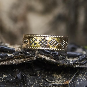 Può includere: Un anello d'oro con un motivo decorativo sulla fascia. L'anello è appoggiato su un pezzo di legno invecchiato.